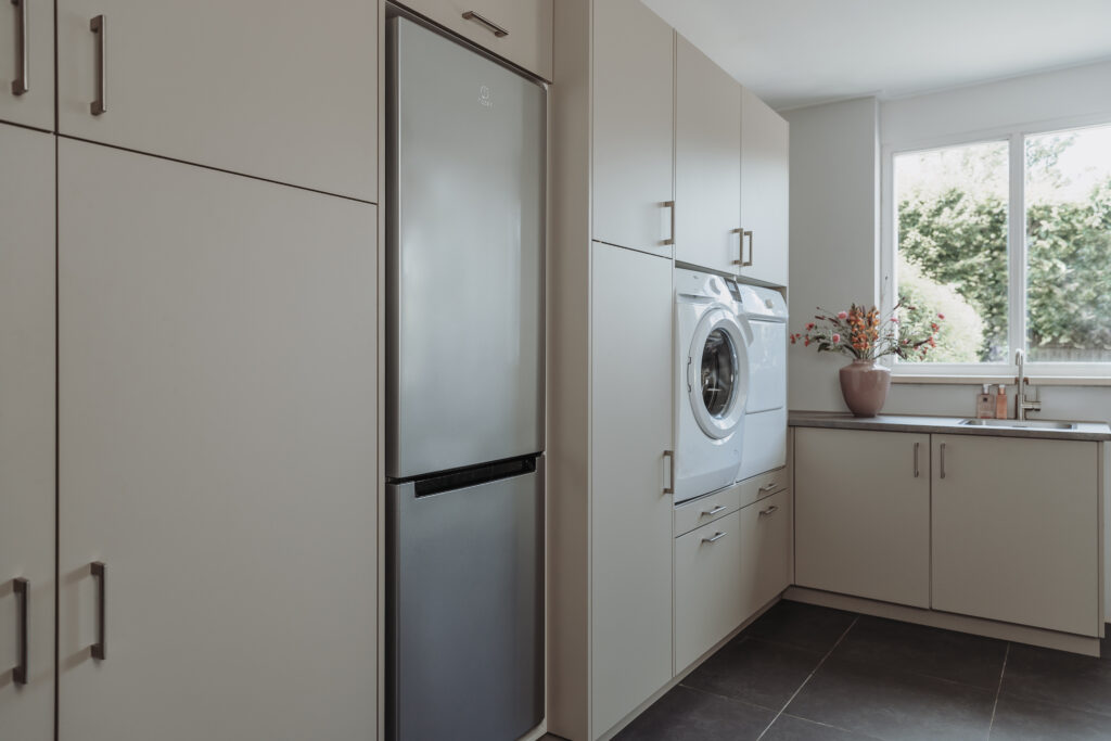 Bijkeuken met ingebouwde kasten, koelkast, wasmachine en droger bij raam.