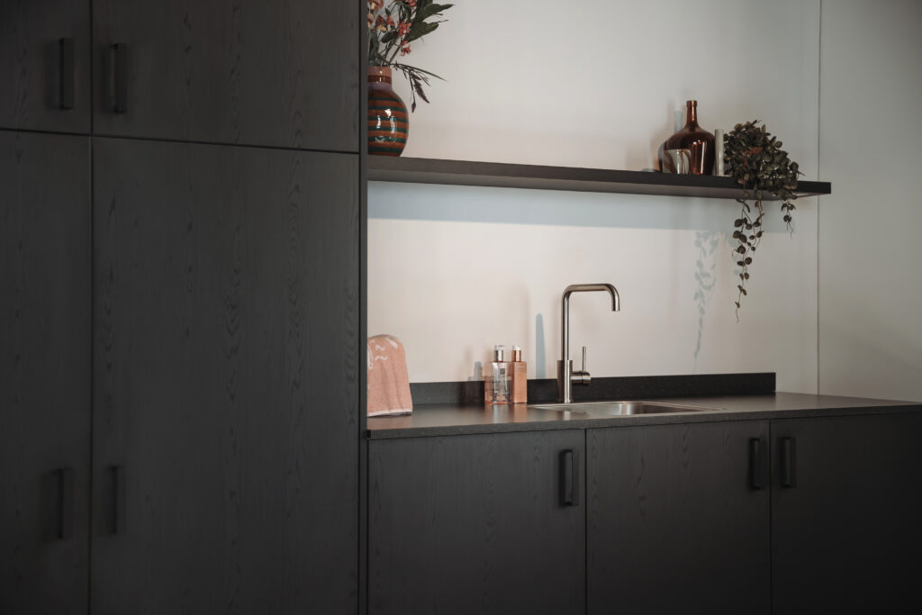 Moderne bijkeuken met donkere kasten, een wastafel en een plank met decoraties.