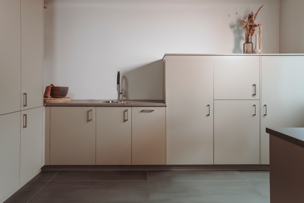 Interieur van bijkeuken model met beige kasten en werkblad, inclusief wastafel en decoratieve accessoires.
